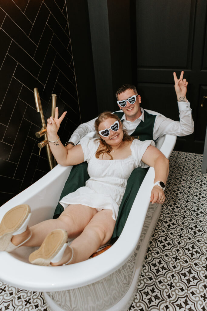 Bride and Groom pose in the bath at Crowcombe Court during a summer wedding in Somerset, captured by a Crowcombe Court wedding photographer.