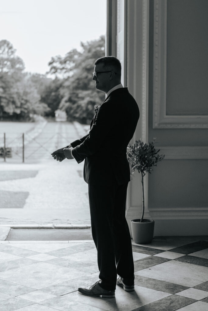 Groom waiting for his bride in the great hall at Crowcombe Court during a summer wedding in Somerset, captured by a Crowcombe Court wedding photographer.
