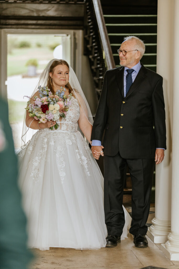 Bride walking down the aisle in the great hall at Crowcombe Court during a summer wedding in Somerset, captured by a Crowcombe Court wedding photographer.