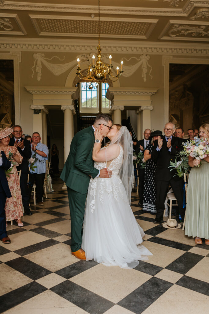 Bride and groom first kiss in the great hall at Crowcombe Court during a summer wedding in Somerset, captured by a Crowcombe Court wedding photographer.